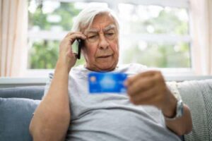 An older man holds up a credit car while speaking on a cellular telephone